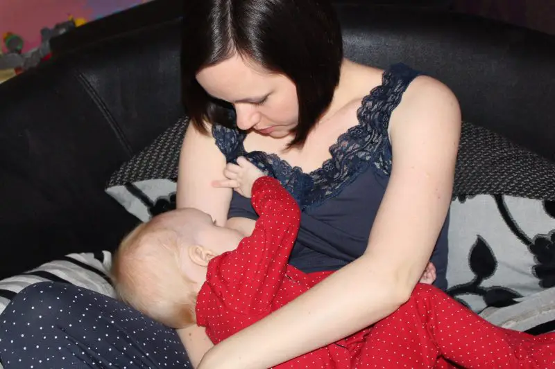 A brunette woman nursing her baby who is in a red sleep suit