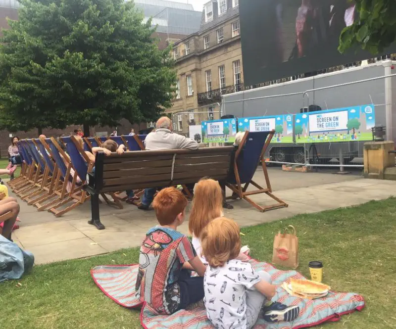 3 children watch a movie with a picnic at screen on the green at Newcastle city centre