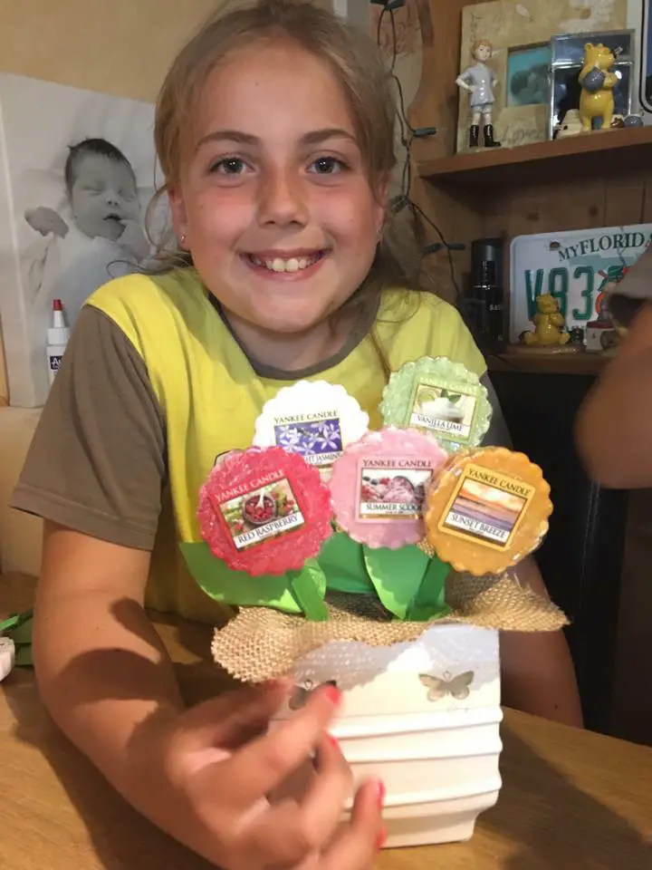 A little girl smiling holding a homemade Yankee candle flower pots gift for her teacher 