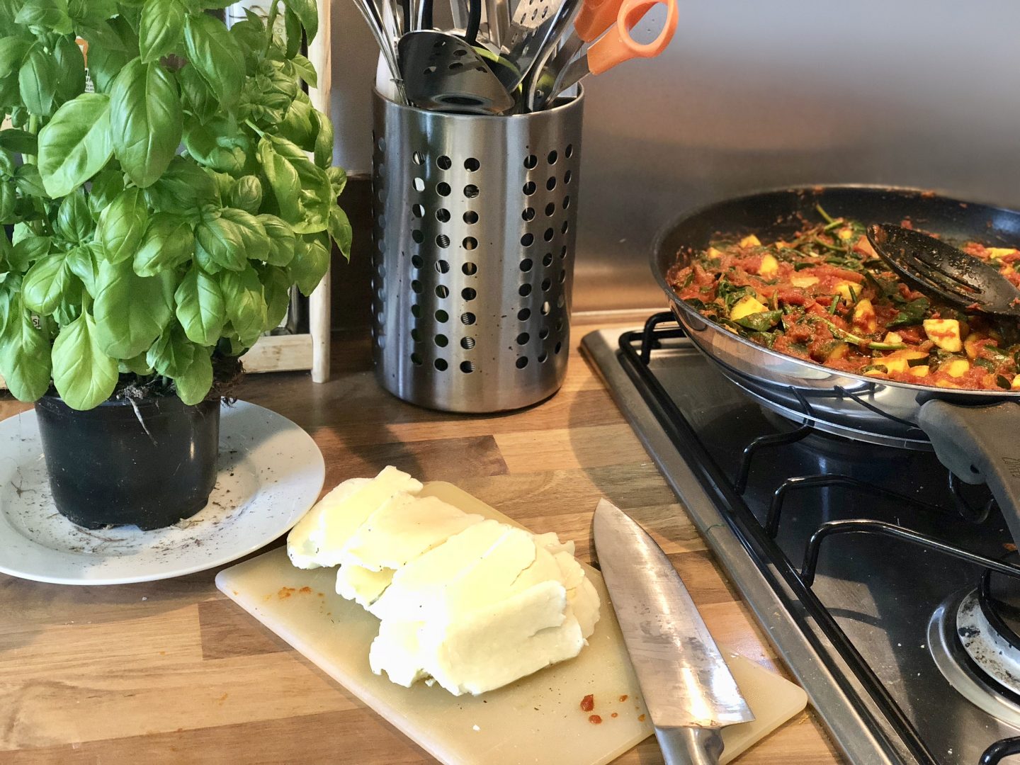 Halloumi hash recipe - sliced halloumi, a pot of basil and a frying pan of courgette and tomatoes 