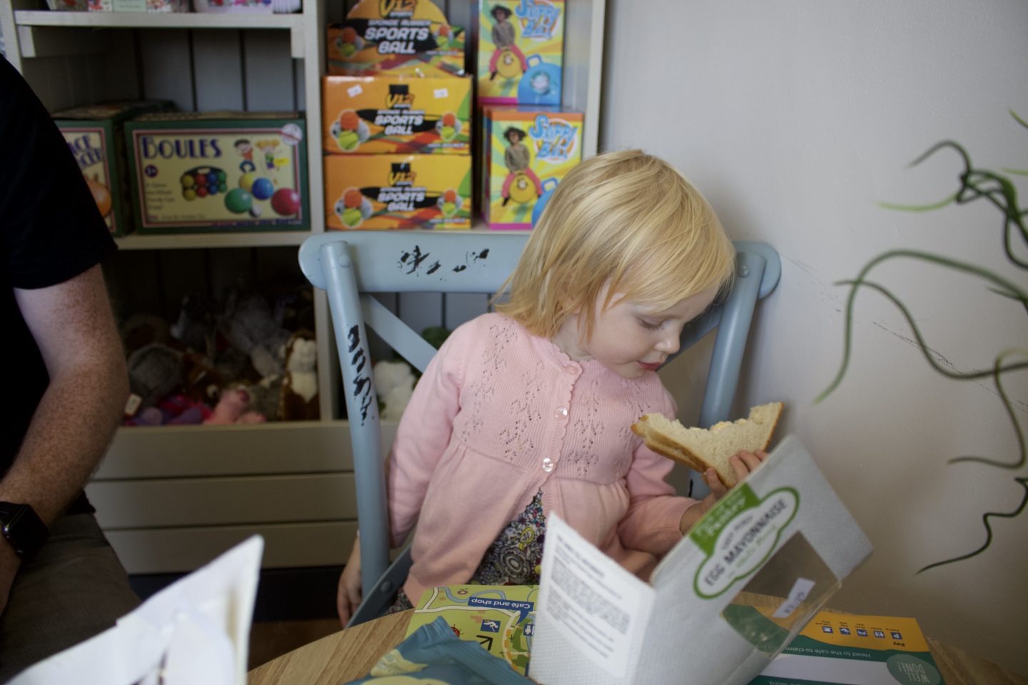 Little girl wearing a pink cardigan eating a sandwich in a cafe