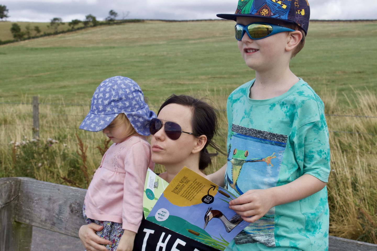 A mother, son and daughter sat on a bench in a field 