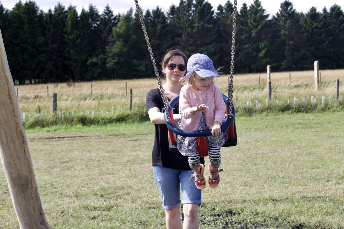 A brunette woman smiling pushing her daughter on a swing