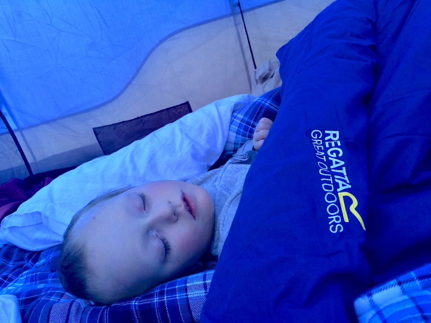 A young boy fast asleep inside his sleeping bag in a tent. 