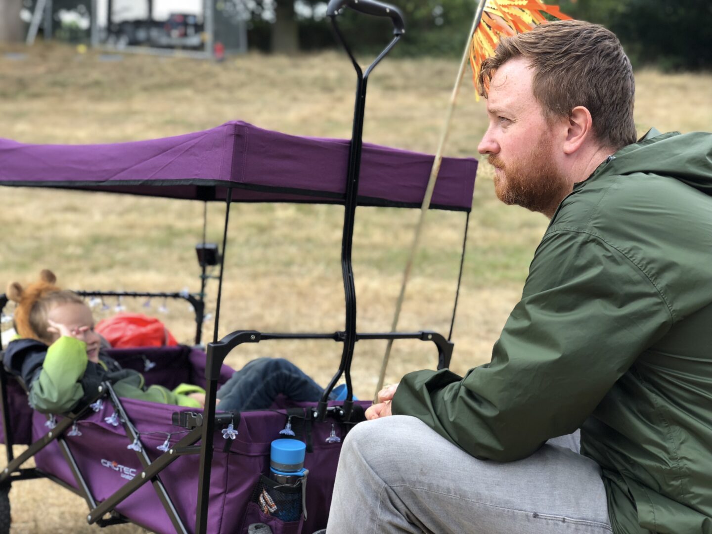 A boy lounges in a festival wagon for kids as his father stares off into the distance. 