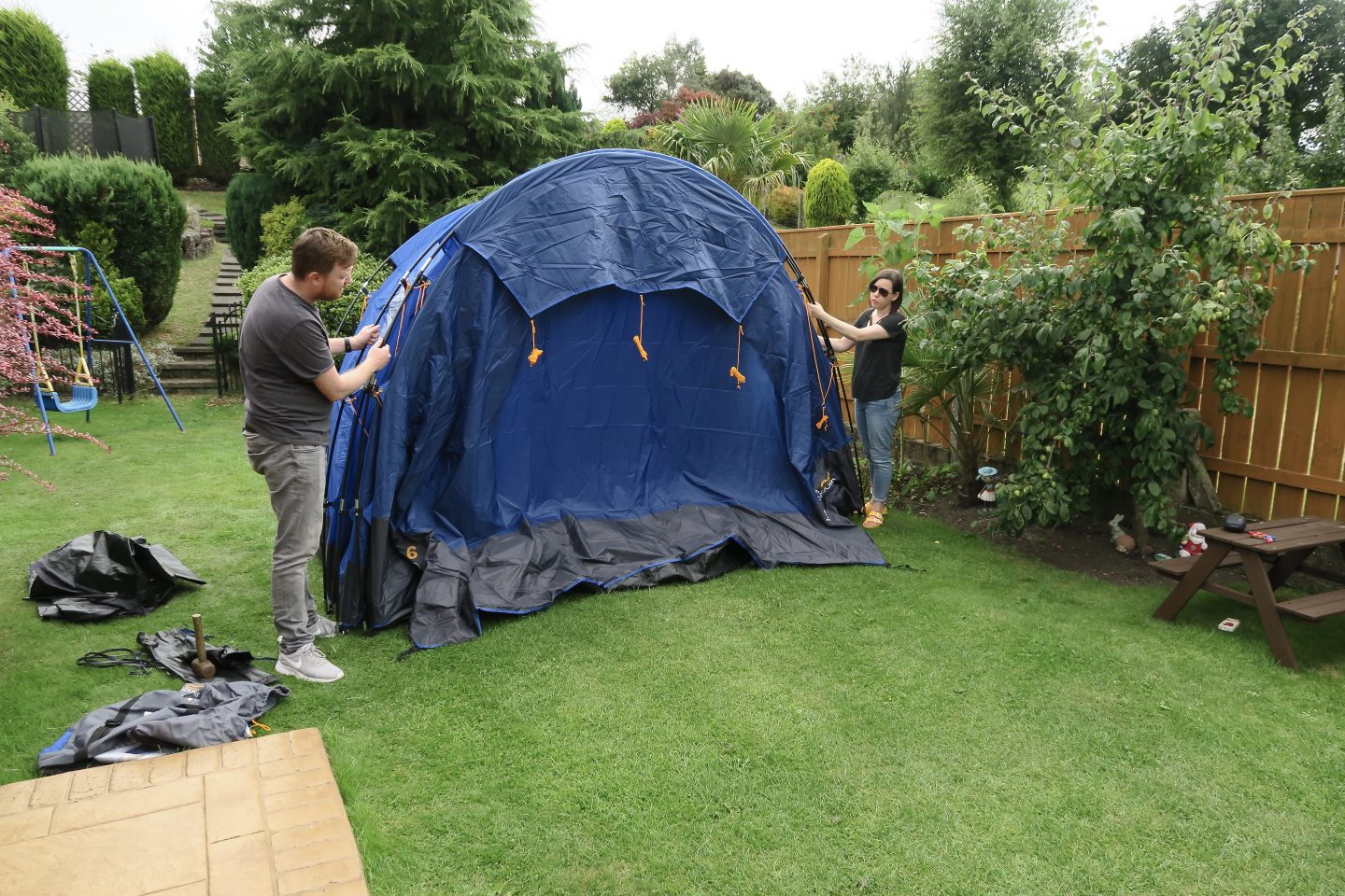 Man and woman putting up a large blue tent in a garden