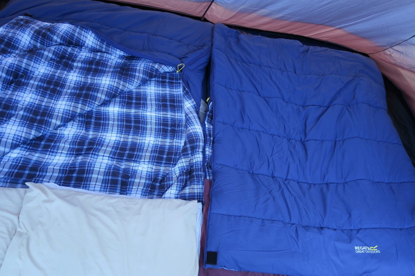 The bedroom set up inside a tent. Shows two double sleeping bags next to each other. They are blue and the inside is a blue check. 