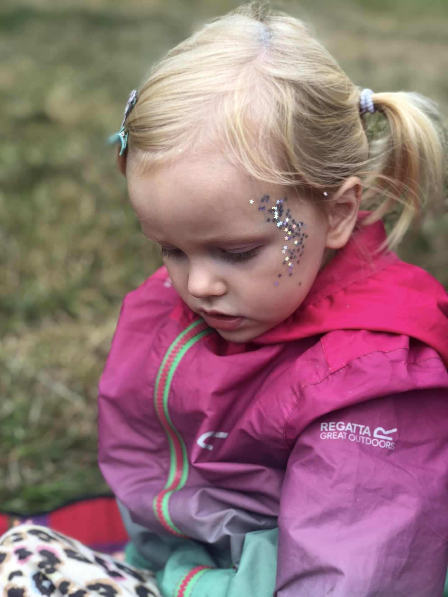 A blonde girl is wearing a waterproof rain jacket and has silver stars on her face. 