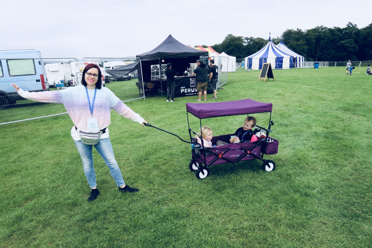 Woman pulling a wagon with kids inside it at a family friendly festival. 