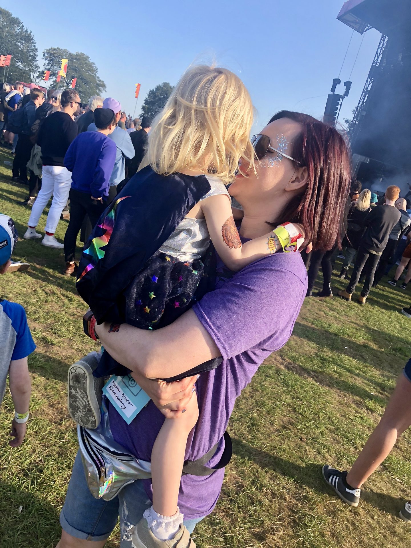 Woman carrying a 3 year old at the main stage of a family friendly festival. 